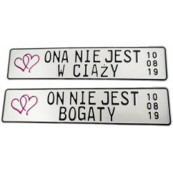 Ona nie jest w ciąży, on nie jest bogaty. Białe tablice rejestracyjne, czarny napis, czerwone serca.